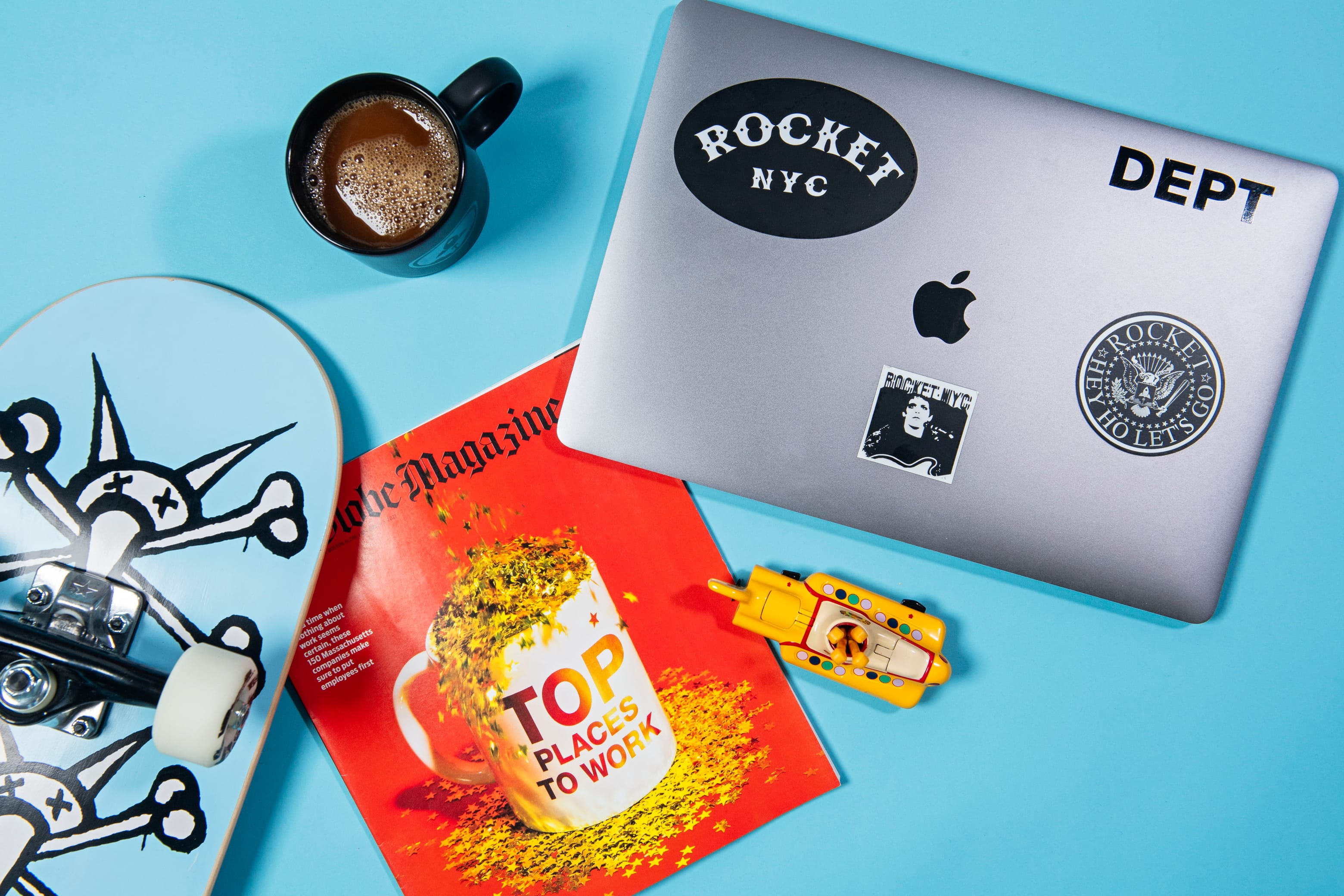 Desk with laptop, coffee, magazine, skateboard, and toy